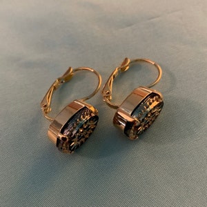 May include: A pair of gold hoop earrings with a dark blue and gold oval-shaped stone. The stones have a textured surface.