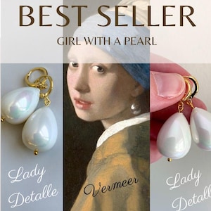 以下が含まれることがあります： 白い真珠のような涙型のチャームが付いた、ゴールドのフープイヤリングのペア。イヤリングは、ヨハネス・フェルメールの有名な絵画「真珠の耳飾りの少女」からインスピレーションを得ています。イヤリングの下には「Lady Detalle」というテキストが書かれています。