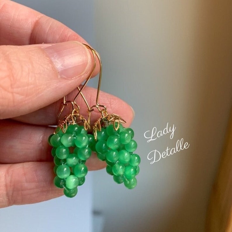 May include: A pair of green grape earrings with gold-tone hooks. The grapes are made of small, round beads.