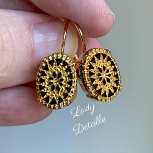 May include: A pair of gold oval earrings with a black center featuring a detailed geometric design. The earrings have a hook closure.