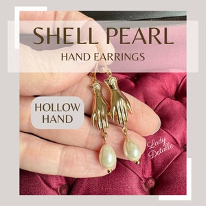 Op de afbeelding: Gouden holle hand oorbellen met een witte parel druppel. De oorbellen worden "Shell Pearl Hand Earrings" genoemd en de handen zijn gelabeld "Hollow Hand".