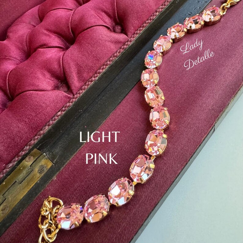 May include: A light pink crystal bracelet with oval-shaped stones and a gold chain. The bracelet is displayed on a burgundy velvet background with the text "LIGHT PINK" and "Lady Detalle".
