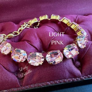 May include: A gold bracelet with light pink oval-shaped crystals. The bracelet is on a burgundy velvet surface.  LIGHT PINK is written in white text on the surface.