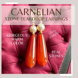 May include: Teardrop carnelian earrings with gold posts and white pearl accents. The earrings are displayed on a red velvet surface. "Gorgeous warm colour" and "Real stones" are written on the image. "Lady Detalle" is written in cursive on the image.