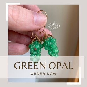 May include: A pair of green opal earrings with gold accents. The earrings are shaped like bunches of grapes.