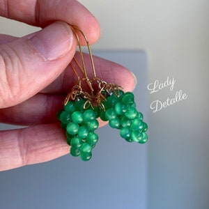 May include: A pair of green glass grape earrings with gold-tone metal accents. The earrings are dangle style and feature a cluster of green glass beads.