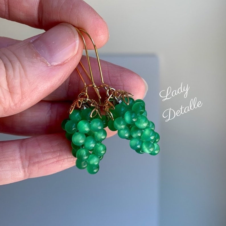 May include: A pair of green glass grape earrings with gold-tone metal accents. The earrings are dangle style and feature a cluster of green glass beads.