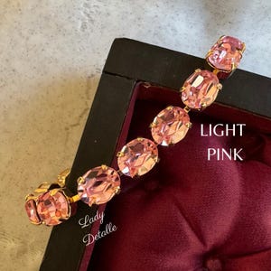 May include: A gold bracelet with light pink oval-shaped rhinestones. The bracelet is displayed in a red velvet lined box. The text "LIGHT PINK" is visible on the box.