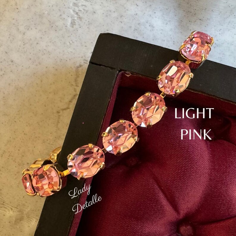 May include: A gold bracelet with light pink oval-shaped rhinestones. The bracelet is displayed in a red velvet lined box. The text "LIGHT PINK" is visible on the box.