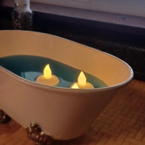 May include: A white bathtub with three tealight candles floating in blue water. The bathtub has gold feet.