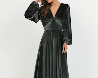 May include: A long, dark green velvet dress with a V-neckline and long sleeves. The dress has a fitted waist and a flowing skirt. The sleeves are gathered at the wrist. The model is wearing the dress in a studio setting.
