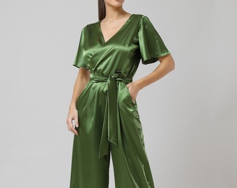Könnte beinhalten: Olivgrüner Satin-Jumpsuit mit V-Ausschnitt, kurzen Ärmeln und weitem Bein. Der Jumpsuit hat einen passenden Stoffgürtel und Taschen. Das Model trägt hochhackige Sandalen. Maße in Zentimetern.