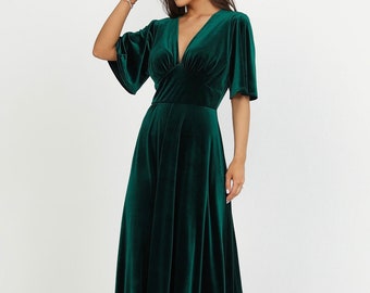 May include: A long, emerald green velvet dress with a V-neckline and short, flared sleeves. The dress has a fitted bodice and a flowing skirt.