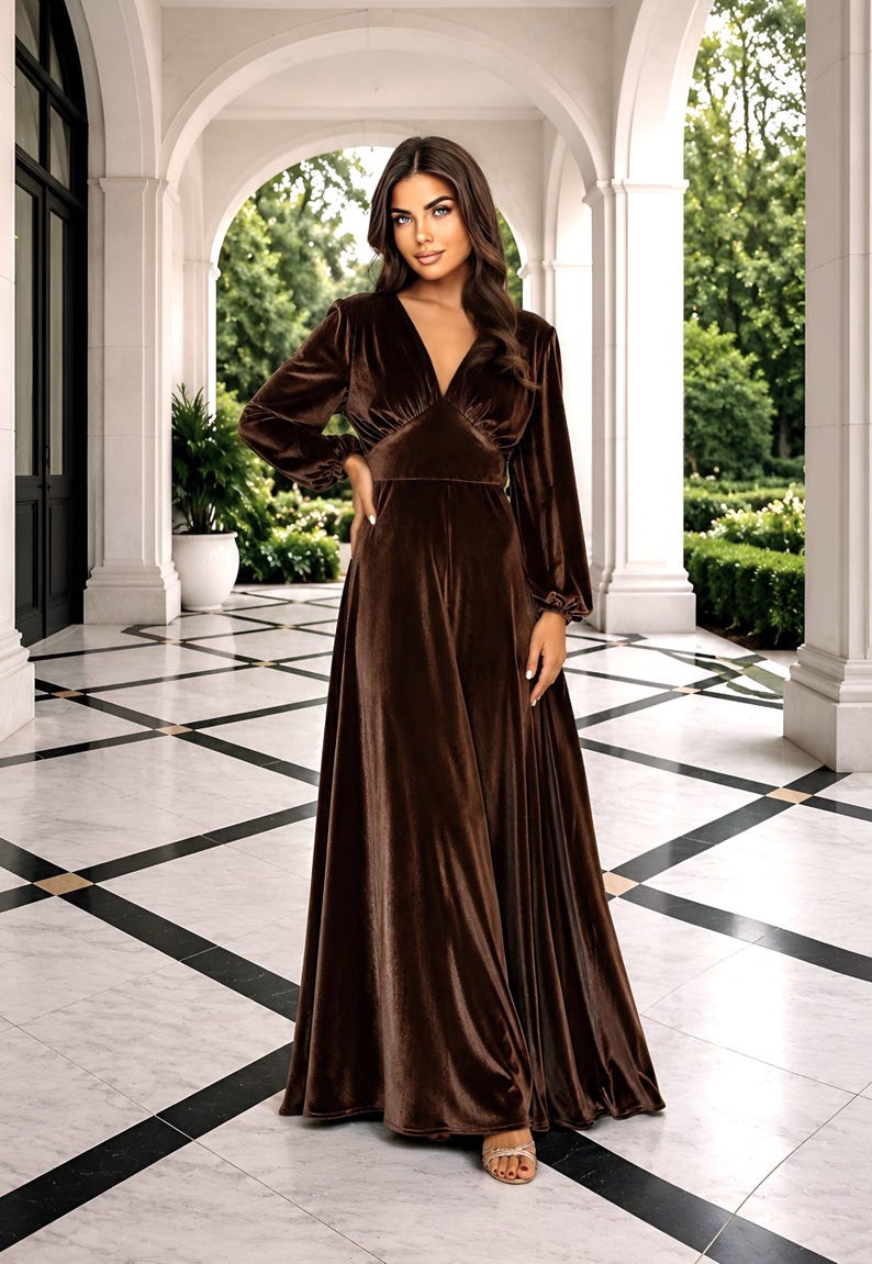 Brown velvet maxi dress with a V-neck and long sleeves. The dress features a fitted bodice and a flowing skirt.