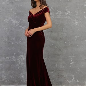Peut inclure: Une longue robe en velours bordeaux avec un décolleté épaules dénudées et un corsage ajusté. La robe a une jupe fluide qui s'étale sur le sol.