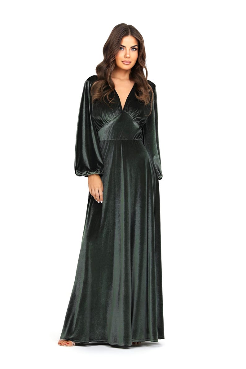 A long, dusty sage velvet dress with a V-neck and long sleeves. The dress features a fitted bodice and a flowing skirt. The sleeves are gathered at the wrist. The floor-length dress is made of a soft, luxurious fabric.