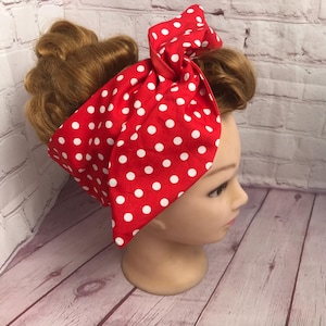 May include: A red fabric headband with white polka dots is tied in a bow on a mannequin head. The headband has a retro design. The mannequin has light brown hair styled in a vintage updo. A classic hair accessory.