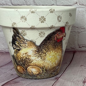 May include: A white ceramic planter featuring a brown and white chicken design with a red comb. The planter has a diamond pattern with a floral design.