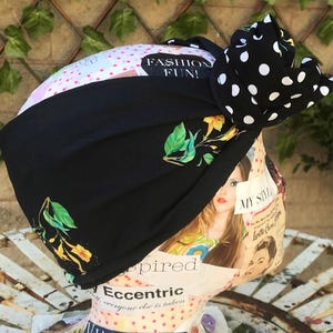 May include: Black turban-style headband with a large bow featuring white polka dots. The headband has a floral design with green leaves and yellow flowers. The text "FASHION FUN!" is visible.