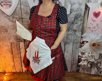 May include: A woman wearing a red plaid apron with a white pocket featuring a candle design. The apron is paired with a black polka dot top. She is also wearing red shoes and holding a white cloth. The background includes decorative elements.