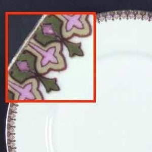 May include: A white ceramic plate with a brown and pink floral border. The border features a repeating pattern of stylized flowers and leaves.