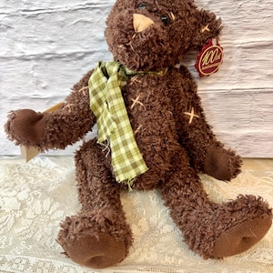 May include: A brown teddy bear with a green and white checkered scarf. The bear has a stitched-on patch that says "100th Anniversary".