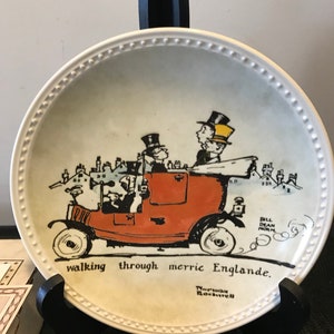 May include: A white ceramic plate with a black and white illustration of a red car with people in it. The plate has a black border with white dots. The text on the plate reads "walking through merrie Englande." and "Norwood Rockwell".