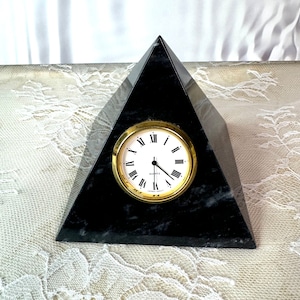 May include: A black marble pyramid clock with gold-tone hands and Roman numeral markings. The clock face reads "Quartz".
