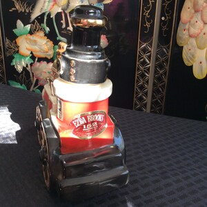 May include: A red, black, and white ceramic decanter shaped like a vintage steam engine. The decanter features a gold label with the text "Ezra Brooks 152" and the words "Kentucky Straight Bourbon Whiskey".