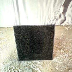 May include: A black square coaster with a textured surface.