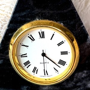 May include: A black marble clock with a gold rim and Roman numeral clock face. The clock face reads "QUARTZ JAPAN-MOV'T".