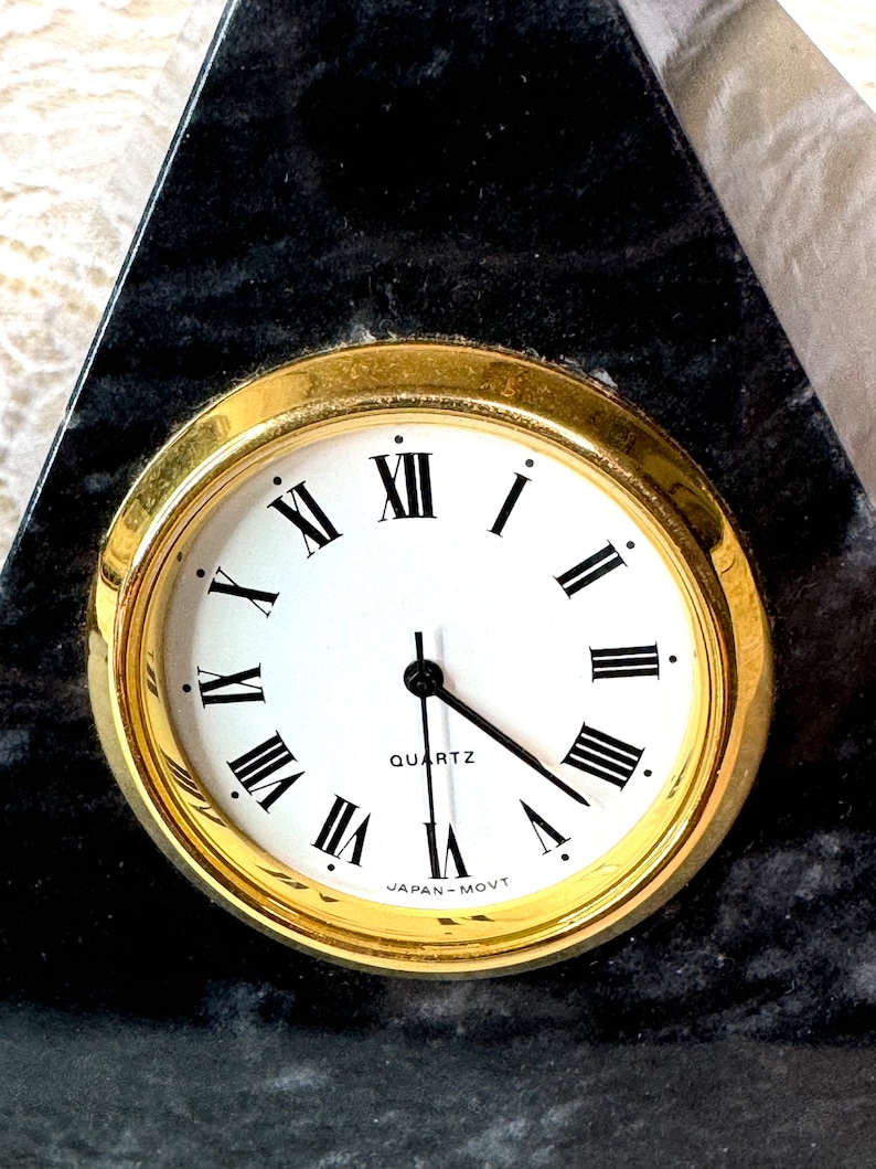 May include: A black marble clock with a gold rim and Roman numeral clock face. The clock face reads "QUARTZ JAPAN-MOV'T".