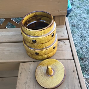 May include: A ceramic cookie jar shaped like a barrel with a wooden grain pattern and brown accents. The lid is separate and has a knob on top.