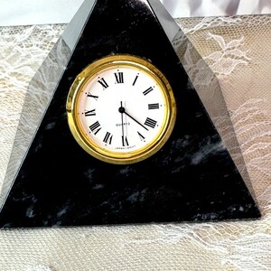 May include: A black marble pyramid clock with gold Roman numeral markings and a white face. The clock reads "QUARTZ" and "JAPAN-MOV'T".