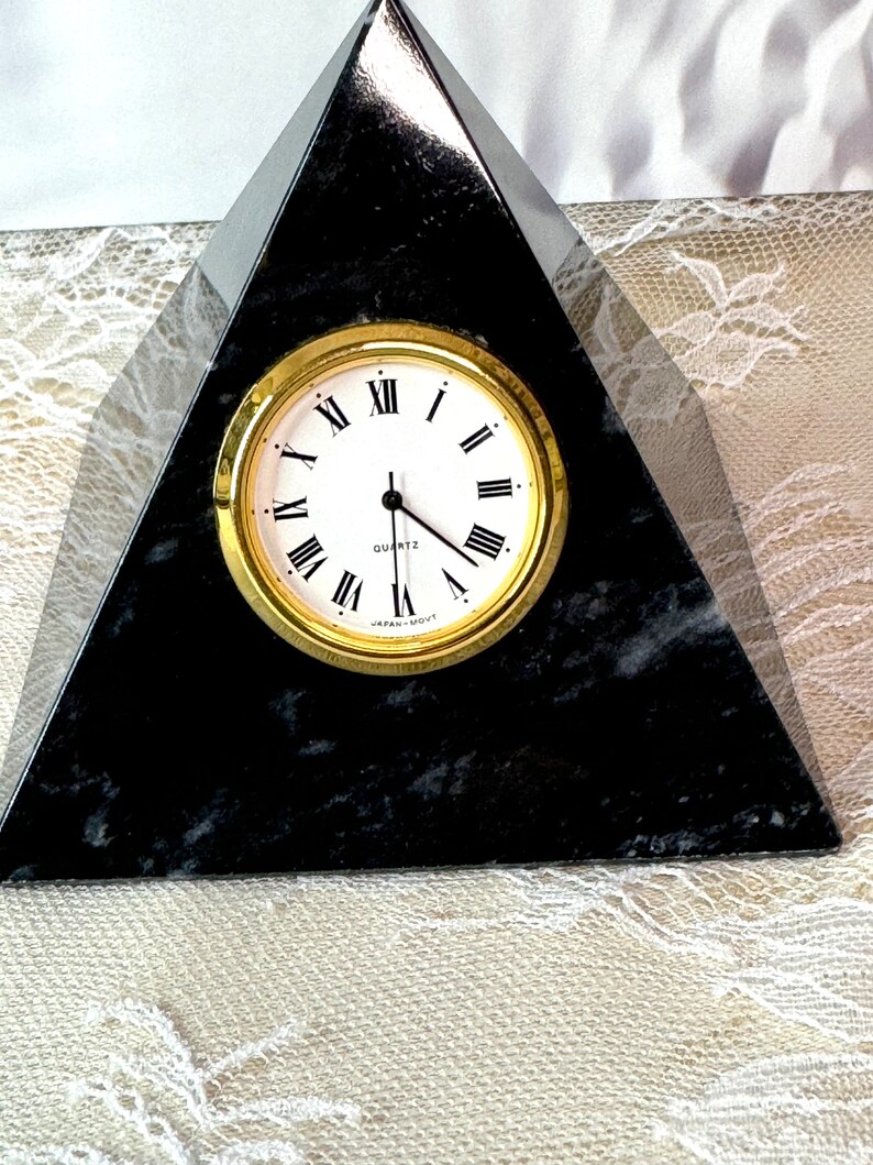 May include: A black marble pyramid clock with gold Roman numeral markings and a white face. The clock reads "QUARTZ" and "JAPAN-MOV'T".