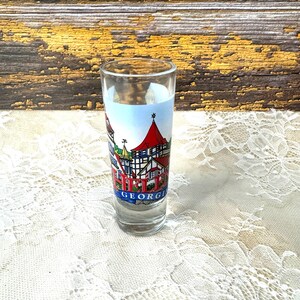 May include: A clear glass shot glass with a colorful illustration of a town with the text "Helga" and "Georgia" printed on the side.