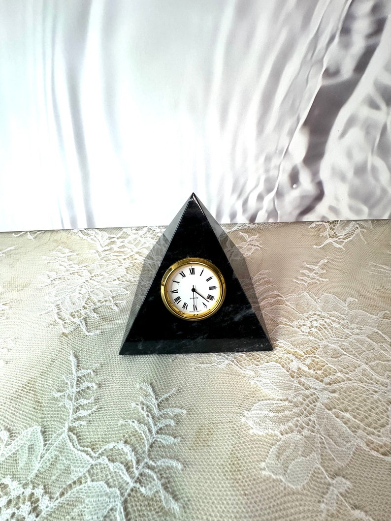 May include: Black marble pyramid clock with gold-tone hands and Roman numeral markings on the clock face.