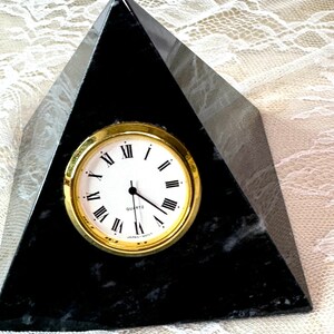 May include: Black marble pyramid clock with gold-rimmed face and Roman numeral markings. The clock face reads "Quartz".