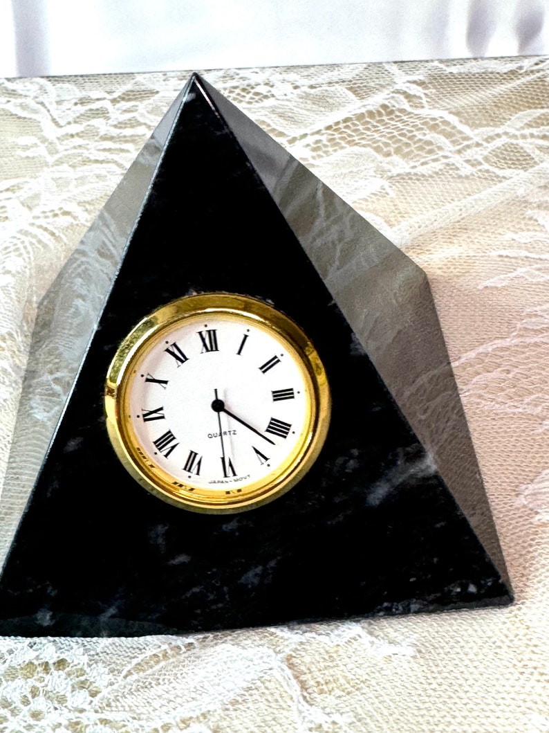 May include: Black marble pyramid clock with gold-rimmed face and Roman numeral markings. The clock face reads "Quartz".