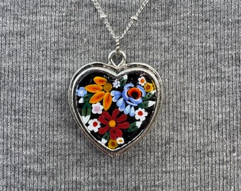May include: A silver heart-shaped pendant necklace with a black background and colorful mosaic floral design.