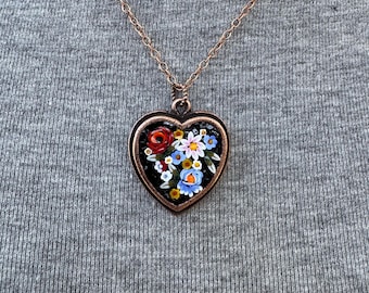 May include: A heart-shaped pendant necklace with a floral design. The pendant is made of black enamel with a copper frame and features a bouquet of red, white, and blue flowers.