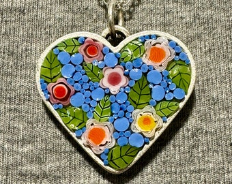 May include: A silver heart-shaped pendant necklace with a mosaic of blue, green, pink, orange, and yellow flowers and leaves.