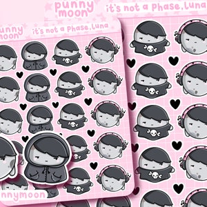May include: A sheet of stickers featuring a cartoon moon character with different expressions and accessories. The moon character is wearing a black hooded jacket, headphones, and a skull and crossbones shirt. The text "punny moon" and "it's not a phase, Luna" is printed on the sheet.