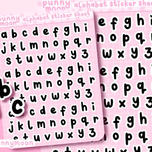 May include: A sheet of alphabet stickers with a pink background and black letters. The letters are in a rounded, bubbly font. The sheet includes the letters a through z and the number 3. The text "punny moon alphabet sticker sheet" is printed at the top of the sheet.