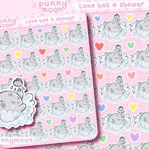 May include: A sheet of stickers featuring a cartoon grey moon character taking a shower. The stickers are on a pink background with a grid pattern. The text "punny moon" and "Luna has a shower" is printed on the sheet.