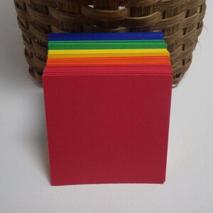 May include: A stack of colorful paper squares in red, orange, yellow, green, blue, and purple. The paper is arranged in a rainbow pattern.