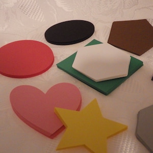 May include: A set of colorful felt shapes, including a red circle, a pink heart, a yellow star, a black oval, a brown hexagon, a white hexagon on a green square, and a gray pentagon.