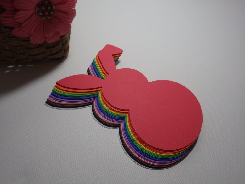 May include: A stack of colorful paper bunny shapes, layered in a rainbow pattern, with the top layer being a bright pink.