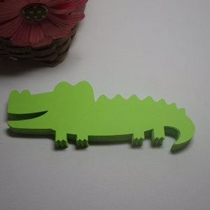 May include: A stack of green paper alligator cutouts. The alligator is facing right and has a toothy grin.
