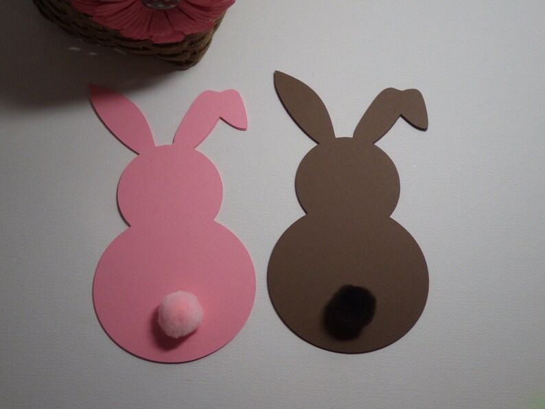 May include: Two paper bunny cutouts, one pink and one brown, with fluffy pom-poms for tails.